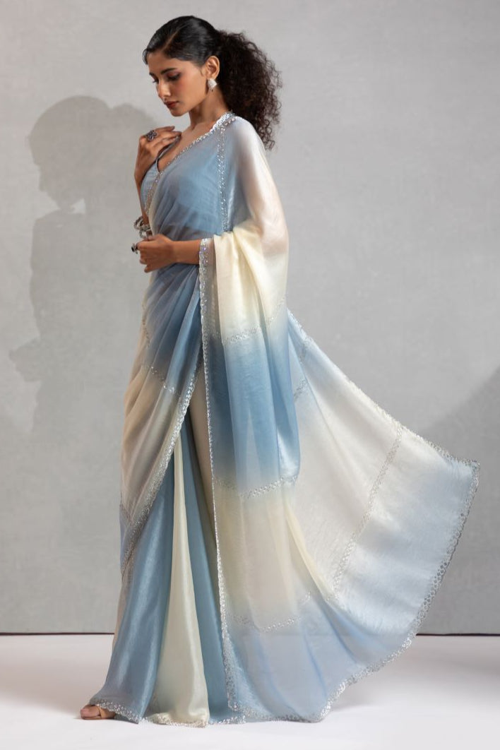 Woman wearing a light blue and white saree against a neutral background