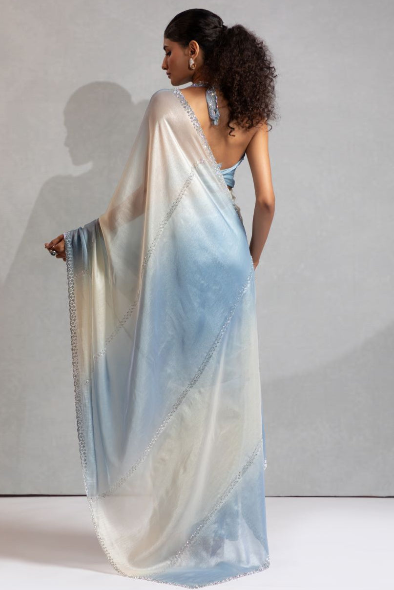 Woman wearing a light blue and white saree against a plain background