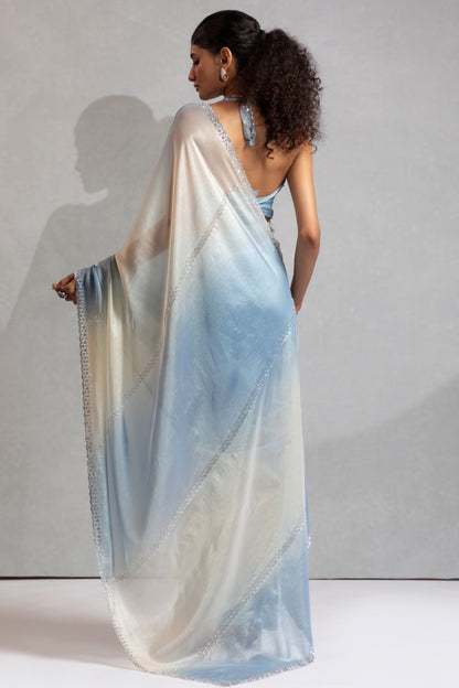Woman wearing a light blue and white saree against a plain background