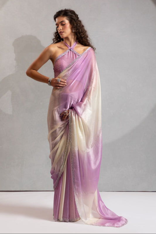 Woman wearing a purple and white saree against a plain background